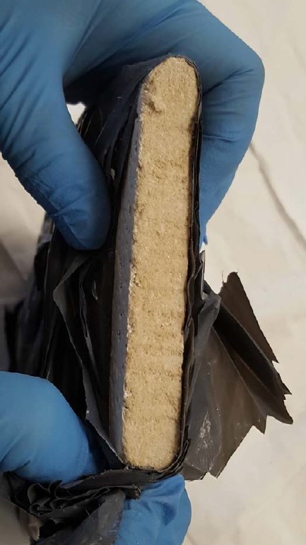 A la imatge veiem una mà amb guants de làtex que sosté un tros no gaire gran de placa de fals sostre.